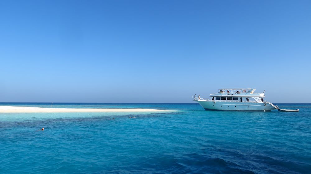 A scenic view of a luxury yacht by a pristine, sandy island in Egypt's vibrant blue waters.