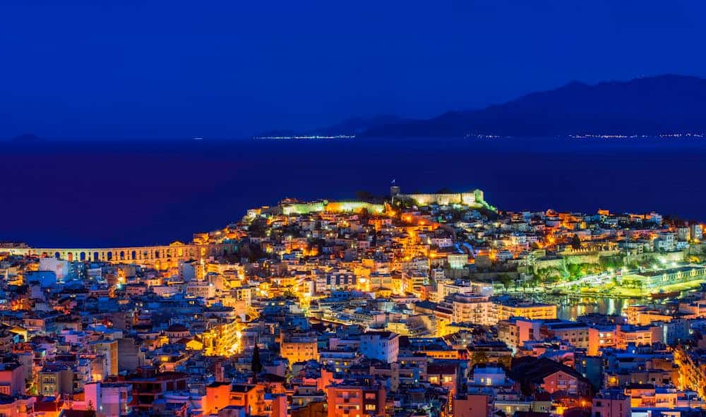 Aerial view of Kavala, Greece, illuminated at night with vibrant cityscape and sea.