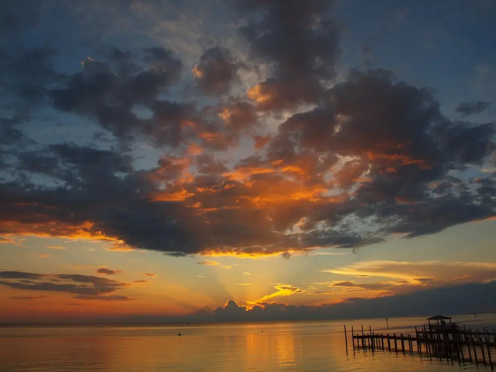 the sun is setting over the ocean with a pier in the foreground at Ocracoke Island, North Carolina