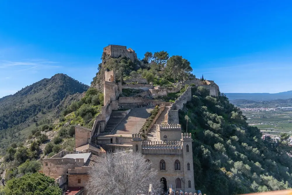 Aerial view of Xàtiva Castle surrounded by lush greenery under a clear blue sky.