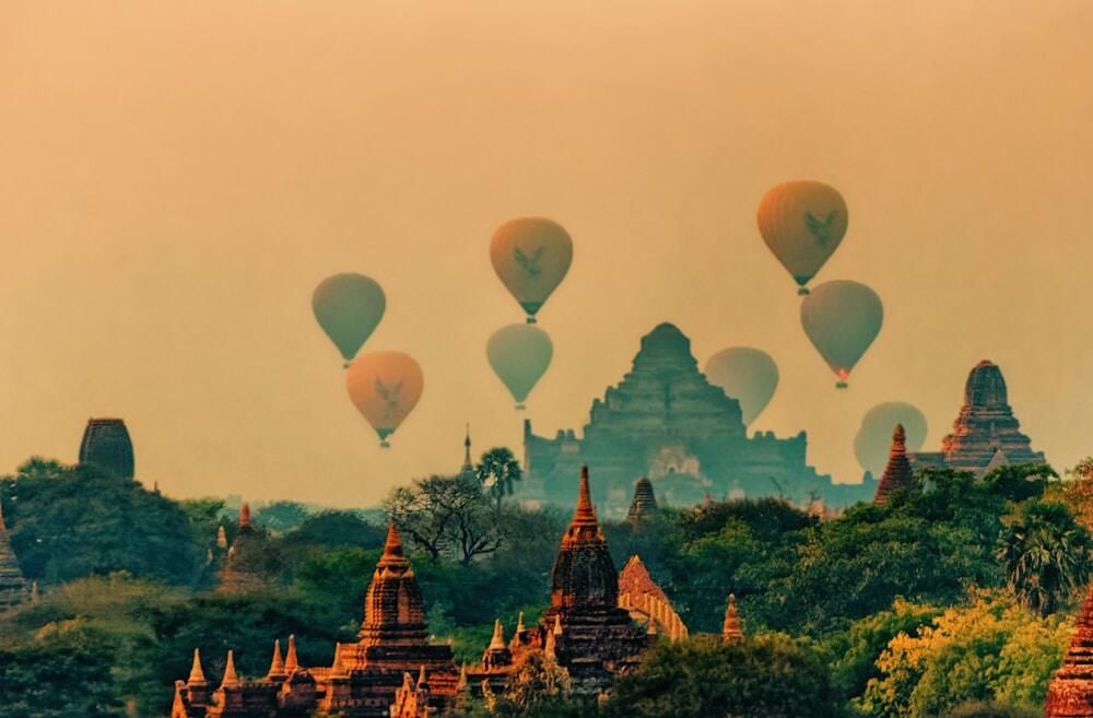 hot air balloons over green trees and golden temples in Myanmar on the sunset