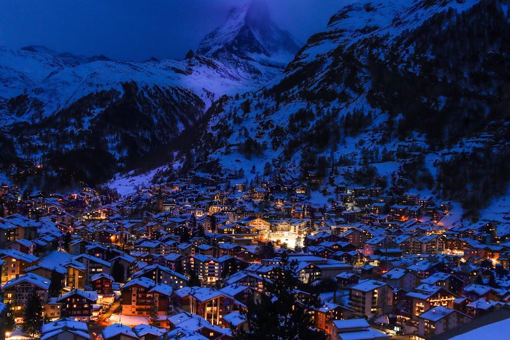 A captivating nighttime view of Zermatt, Switzerland, with illuminated houses and snow-covered mountains.
