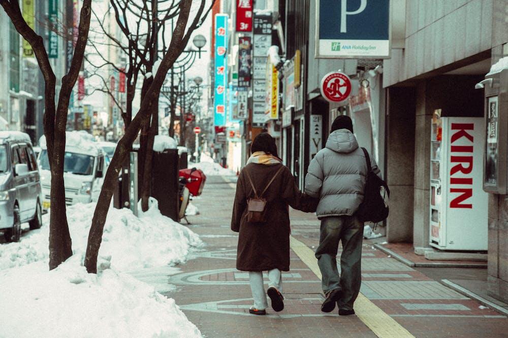 Couple walking hand in hand on a snowy sidewalk in Sapporo, Japan.