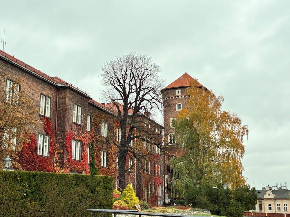 Wawel Castle in Kraków showcasing vibrant autumn foliage against a cloudy sky.