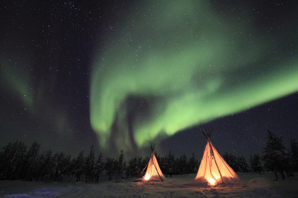 lighted tipi tent under green Northern lights in Yellowknife, Canada