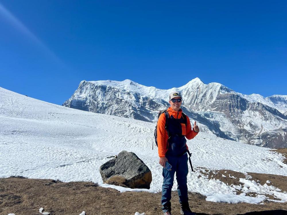 Pem Chhotar Sherpa, a professional trekking guide, standing on a snow-covered section of the Everest Base Camp trail with the high Himalayan peaks in the background.