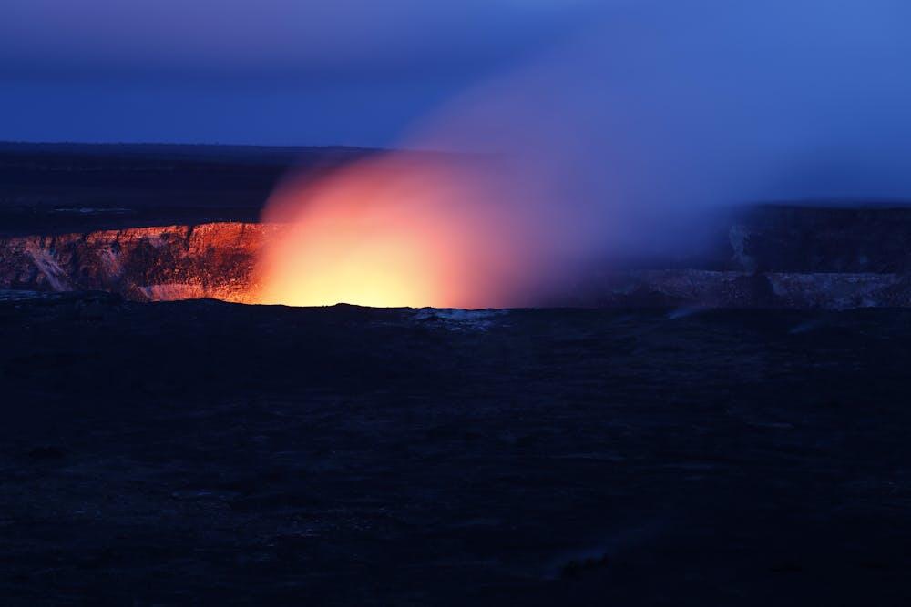 A stunning nighttime view of Kīlauea volcano eruption, with fiery lava glowing against the dark sky.
