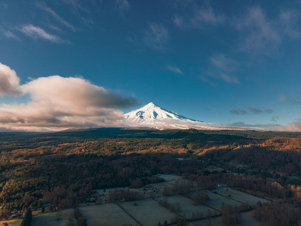 A stunning aerial view of snowcapped Villarrica Volcano with vast forests and fields in Chile.
